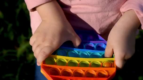 Lapsi leikkii kadulla pop se aistillinen lelu. Tyttö painaa värikkäitä sateenkaaren pehmeä silikoni kuplia. Stressin ja ahdistuksen lievittäminen. Muoti fidgeting peli - Materiaali, video