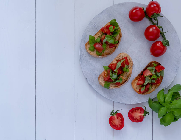 Three bruschetta with tomatoes and fresh basil on a white wooden board - Valokuva, kuva
