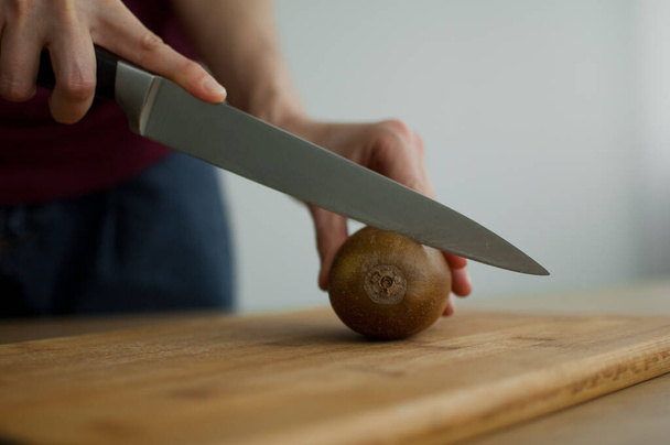 Female hands is cutting a fresh ripe golden kiwi fruit on a cut wooden board. Exotic fruits, healthy eating concept - Photo, Image