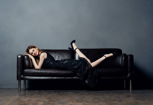 jolie femme posant sur canapé en robe noire style de vie - Photo, image