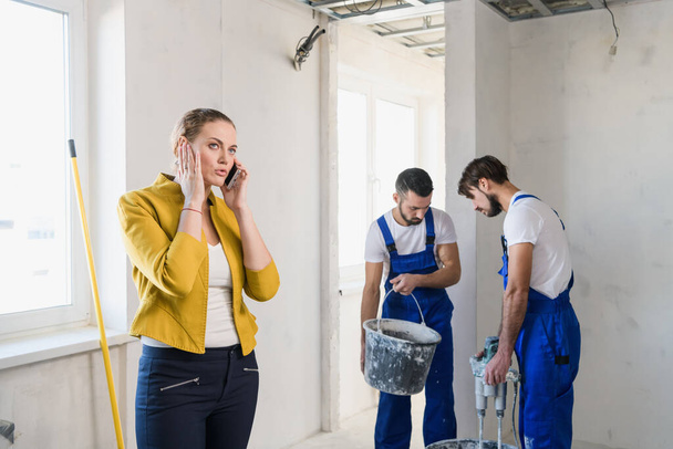 Будівельники ремонтують кімнату, жінка говорить по телефону
 - Фото, зображення