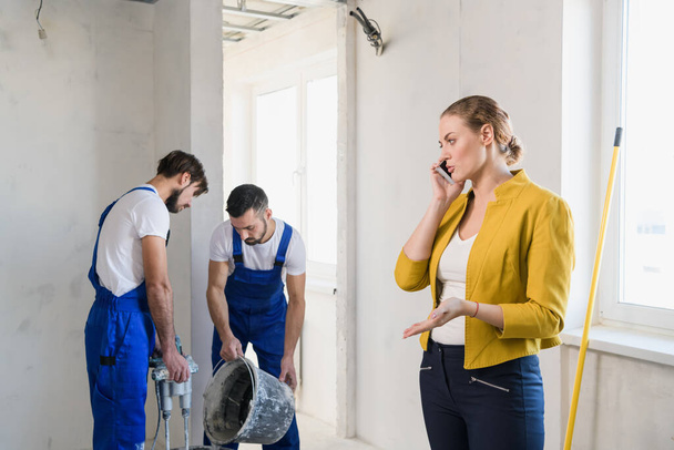 Builders are renovating a room, a woman speaks on the phone - Φωτογραφία, εικόνα