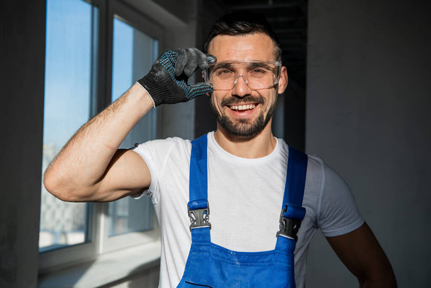 Reparateur in blauwe overall en bril glimlachend - Foto, afbeelding