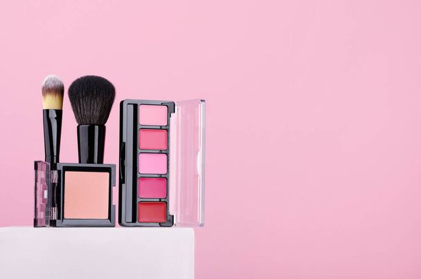 Set of cosmetic products lipsticks, powder, makeup brushes on pink background. Beauty products for professional fashionable makeup by a make-up artist. Women's accessories for skin care. Copy space. - Photo, Image