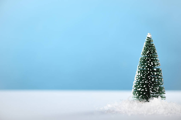 Artificial little Christmas tree in the snow on a blue background. Congratulation and celebration of the winter seasonal holiday, new year. Minimal composition, snowy scene, backdrop. Copy space. - Photo, Image