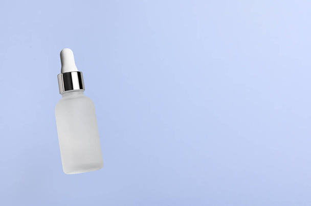 White translucent bottle with dropper with a beauty serum on a blue background. Glass packaging for cosmetic product, essential aroma oil. Skin care, hydration and nutrition with collagen. Levitation. - Foto, Bild