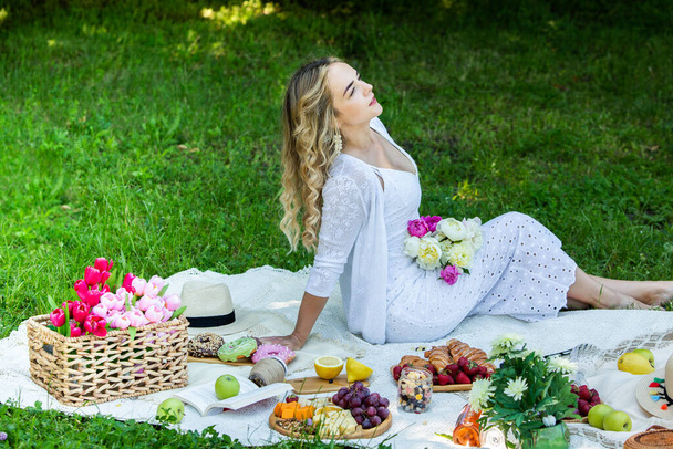 Parkta dinlenen güzel bir kadın piknik battaniyesine oturmuş meyve ve şarapla.  - Fotoğraf, Görsel