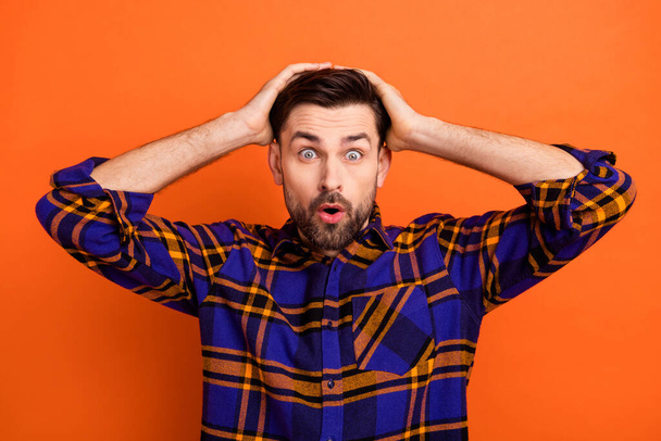 Photo of young guy hands touch head amazed shocked surprised fake novelty news isolated over orange color background - Fotó, kép