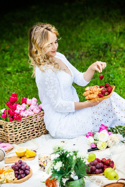 Красива жінка відпочиває в парку, сидячи на пікніку з фруктами і вином
.  - Фото, зображення