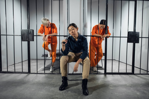Ασιατική γυναικεία φυλακή. Στο κελί υπάρχουν δύο νεαρά κορίτσια καταδικασμένα για ποινικό αδίκημα και μια γυναίκα δεσμοφύλακας με στολή φρουρού. - Φωτογραφία, εικόνα