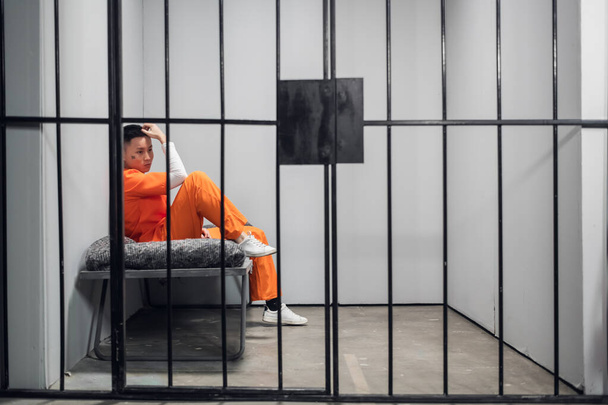 Ασιάτης εγκληματίας με τατουάζ στο πρόσωπό του σε ένα κελί μετανοώντας για το έγκλημα. Κατάθλιψη κρατουμένου στη φυλακή. - Φωτογραφία, εικόνα
