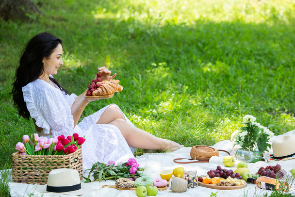 美しいブルネットの女性がピクニック毛布の上に座って公園で休んでいます。自然の中でリラックス. - 写真・画像
