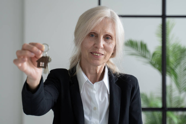 Elderly woman real estate agent with the keys to the apartment in her hands - Foto, imagen