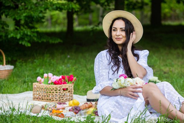Schöne brünette Frau ruht sich im Park auf einer Picknickdecke aus. Entspannung in der Natur. - Foto, Bild