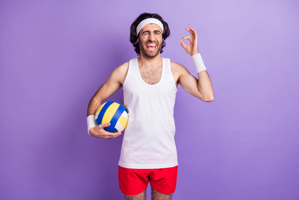 Photo of optimistic brunette guy show okey hold ball wear spectacles white singlet isolated on lilac color background - Foto, immagini