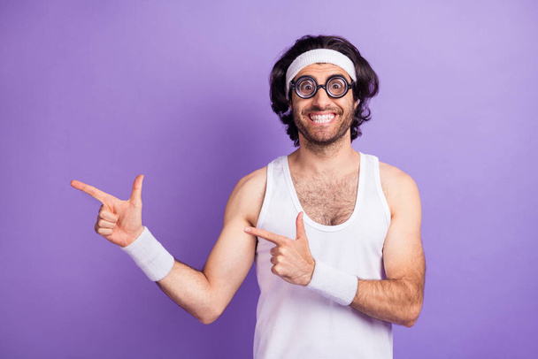 Photo of optimistic brunette guy point empty space wear big spectacles white singlet isolated on lilac color background - Valokuva, kuva