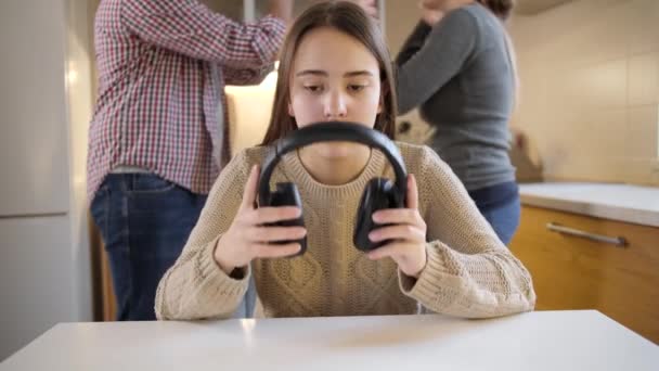 Adolescente fermant les oreilles avec des écouteurs pendant que les parents se disputent, crient et crient en arrière-plan. Violence familiale, conflits et problèmes relationnels - Séquence, vidéo