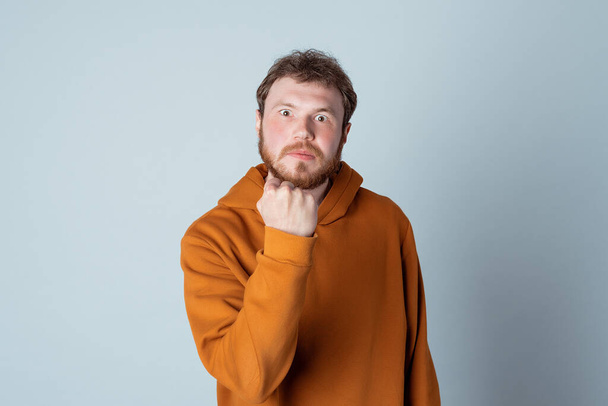 Angry bearded young man raising fists frustrated and furious, standing in stylish hoodie against studio gray background. True human reactions, emotions and feelings. Rage and aggressive concept - Foto, Imagen