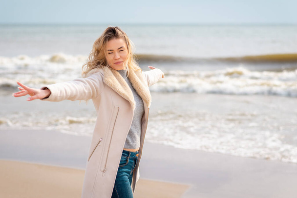 Relaxed woman, arms rised, enjoying spring sun, on a beautiful beach. Young lady outstretched hands feeling free, relaxed and happy. Concept of vacations, freedom, happiness, enjoyment. - Foto, imagen