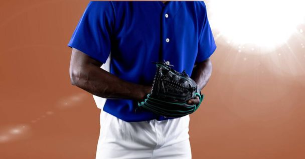 Mid section of african american male baseball pitcher against spot of light on orange background. sports tournament and competition concept - Foto, Imagem