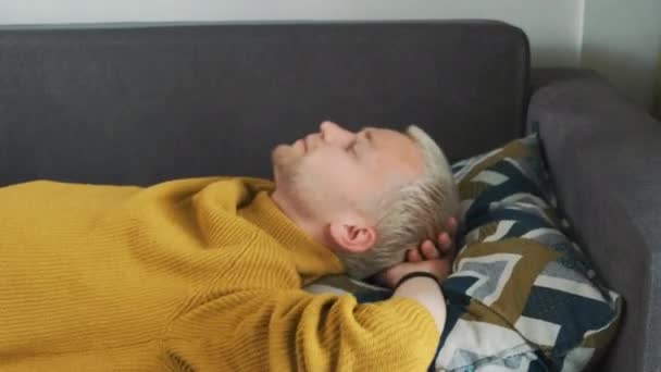 Νεαρός Ευρωπαίος εξαντλημένος ή βαριεστημένος άνδρας πέφτει κυριολεκτικά στον καναπέ-μαξιλάρι μετά από μια σκληρή εργάσιμη ημέρα και αποκοιμιέται. - Πλάνα, βίντεο