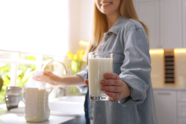 Young woman with gallon bottle of milk and glass at white countertop in kitchen, closeup - Foto, immagini