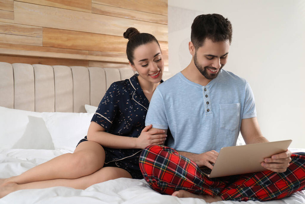 Happy couple in pajamas with laptop on bed at home - Valokuva, kuva