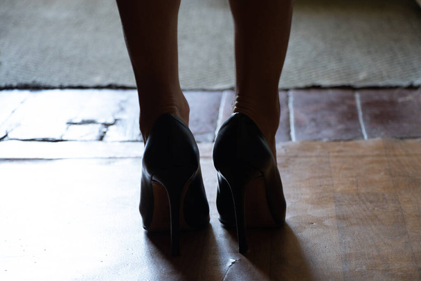 γυναικεία πόδια στο πάτωμα στο σκοτάδι στο σπίτι με μαύρα ψηλοτάκουνα παπούτσια, ένα κορίτσι στέκεται στο πάτωμα στο σπίτι με παπούτσια - Φωτογραφία, εικόνα