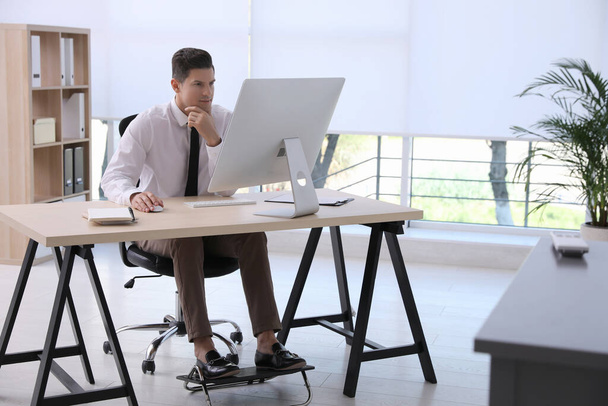 Человек, использующий подножку во время работы на компьютере в офисе - Фото, изображение