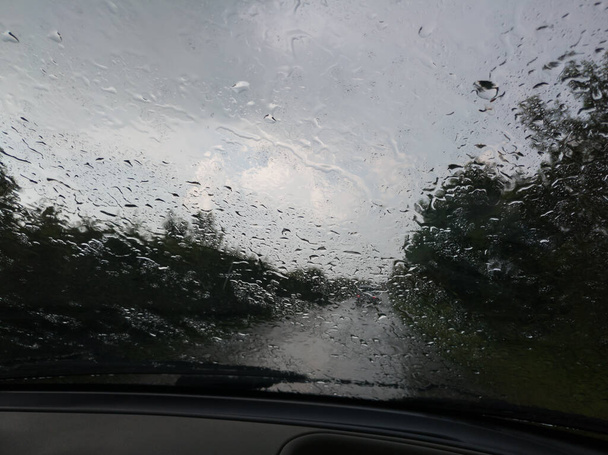 Автомобиль лобовое стекло покрыто капли дождя во время вождения, опасность из-за низкой видимости, кабины автомобиля во время осадков - Фото, изображение