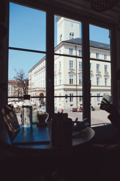 view of city center square of old european city through the window of restaurant laptop on the table freelancer workplace - Foto, Imagem