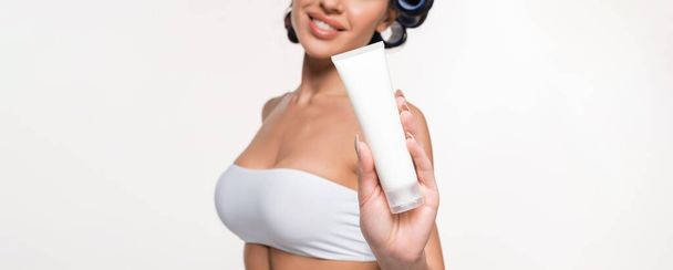 partial view of young woman in curlers and top showing cream tube isolated on white, banner - Photo, Image