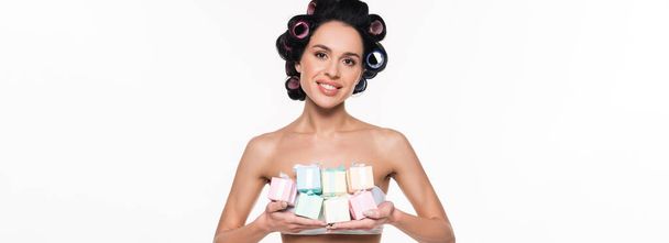 cheerful young woman in curlers holding small gift boxes in hands isolated on white, banner - Photo, Image
