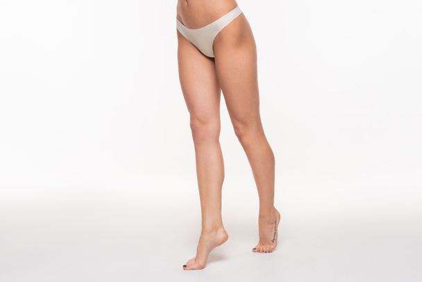 partial view of young woman in beige panties and with fit legs standing on tiptoes on white - Foto, imagen