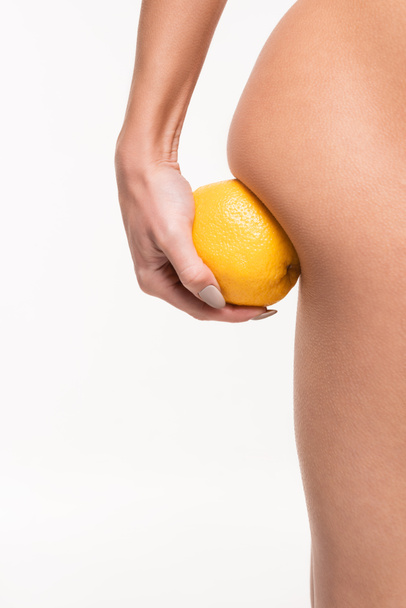 vista de cerca de la mujer joven haciendo masaje anti-celulitis de nalga con naranja aislado en blanco - Foto, Imagen