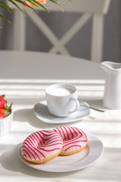 Donuts zum Frühstück. schöne gestreifte Donuts auf einem weißen Teller mit einer Tasse frischen Cappuccino auf dem Tisch. romantischer Morgen, Brunch zu Hause - Foto, Bild