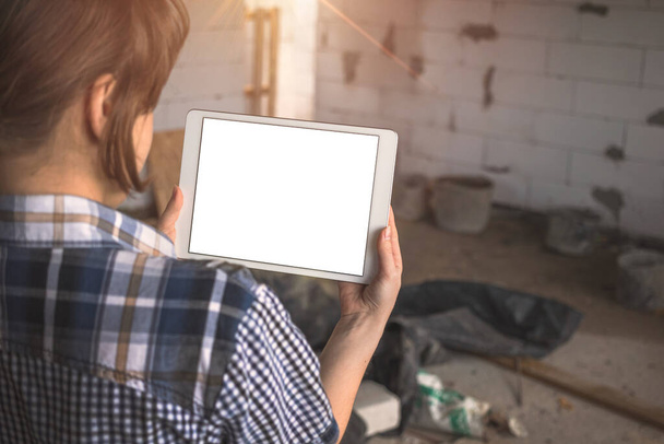 Girl with a tablet in front of an unfinished house, repair, construction concept, copy space  - 写真・画像