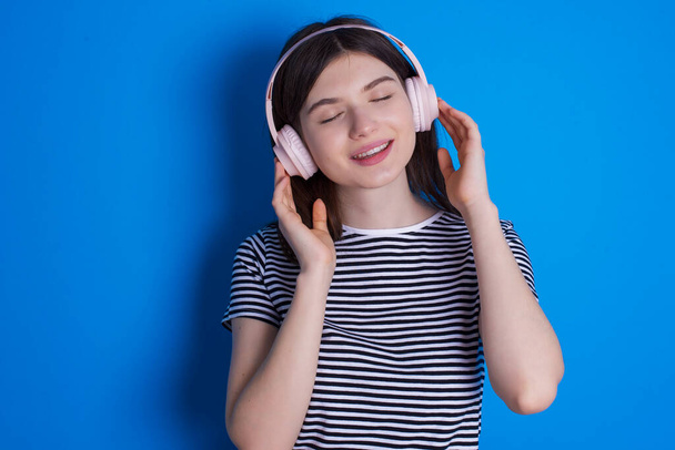 young woman with headphones on her head, listens to music, enjoying favourite song with closed eyes, holding hands on headset. - Foto, Imagen