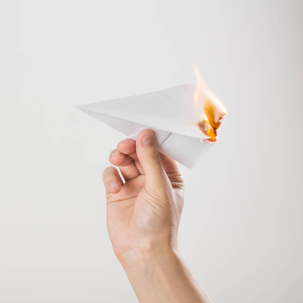 A hand holds a burning paper airplane. Close up. Isolated on a gray background. - Zdjęcie, obraz