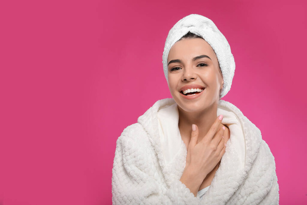 Happy young woman in bathrobe with towel on head against pink background, space for text. Washing hair - Foto, afbeelding
