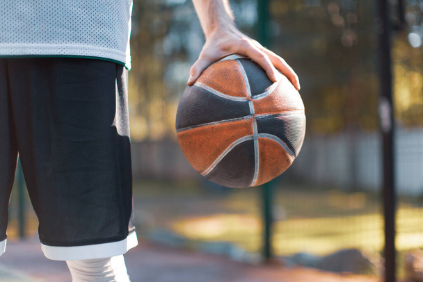 American basketball. Close-up of male professional basketball player holding ball outdoor in sunlight - Fotografie, Obrázek