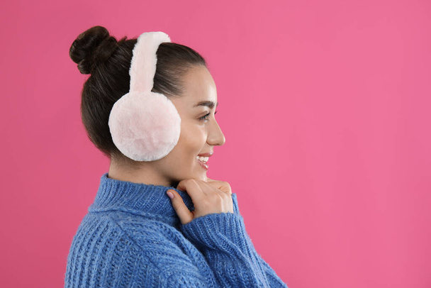 Beautiful young woman wearing earmuffs on pink background. Space for text - Фото, изображение