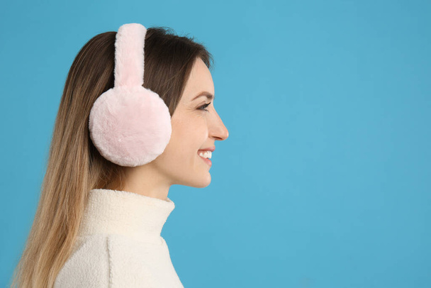 Happy woman wearing warm earmuffs on light blue background, space for text - Photo, Image