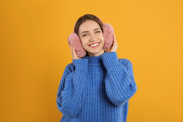 Happy woman wearing warm earmuffs on yellow background - Фото, изображение