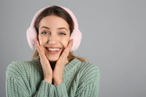 Happy woman wearing warm earmuffs on grey background, space for text - Фото, изображение