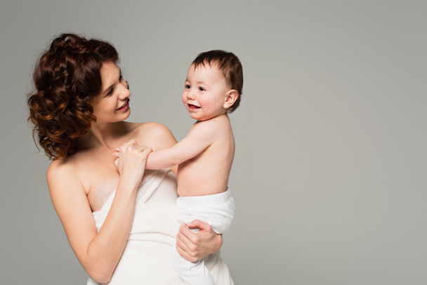 mãe feliz em toalha segurando nos braços filho em meias de bebê isolado em cinza - Foto, Imagem
