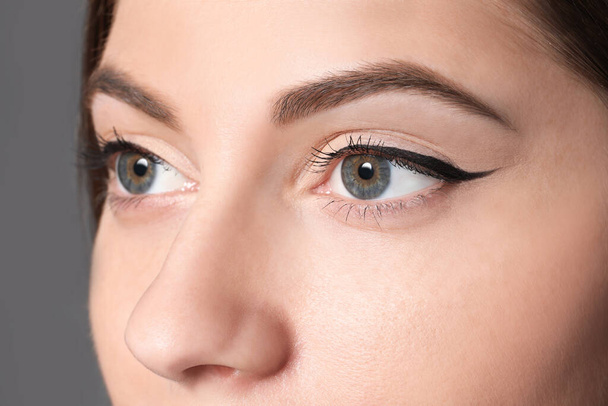 Beautiful woman with black eyeliner on grey background, closeup - Foto, imagen