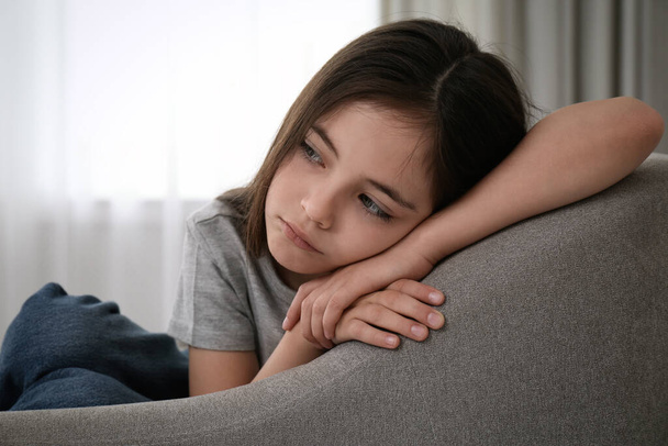 Sad little girl sitting on sofa indoors - Valokuva, kuva