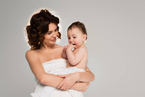 curly mother wrapped in towel holding baby boy in arms isolated on grey  - Photo, Image