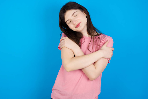 young brunette woman hugging oneself happy and positive, smiling confident. Self love and self care - Photo, image